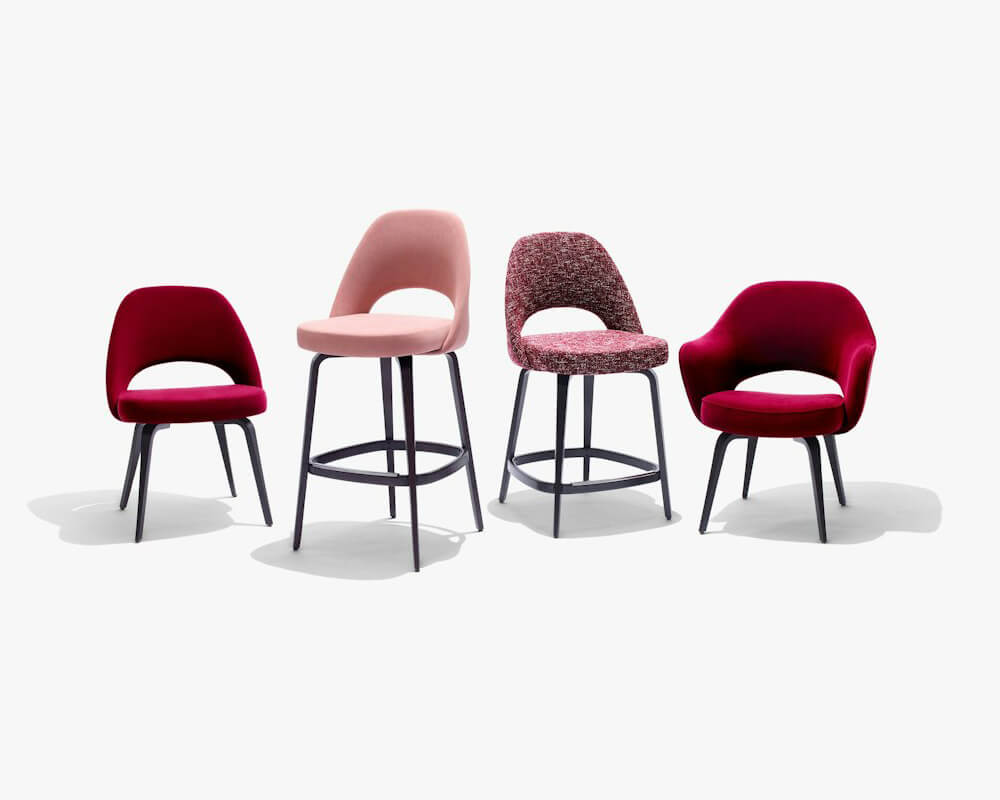 Saarinen wooden legs Barstool and side chairs next to them in a white background