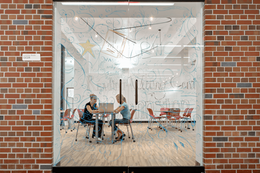 two universiti students behind a class window siting with a laptop