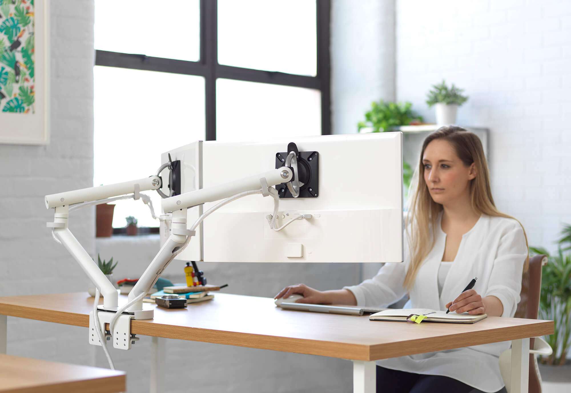 Flo Dual Ergonomic Monitor Arm back and a person looking at the monitor screens