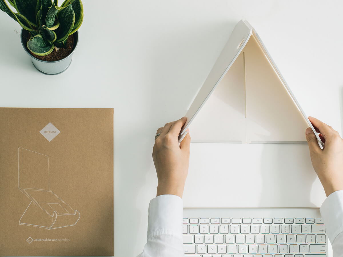a person setting up an Oripura Foldable Laptop Stand on top of a white table