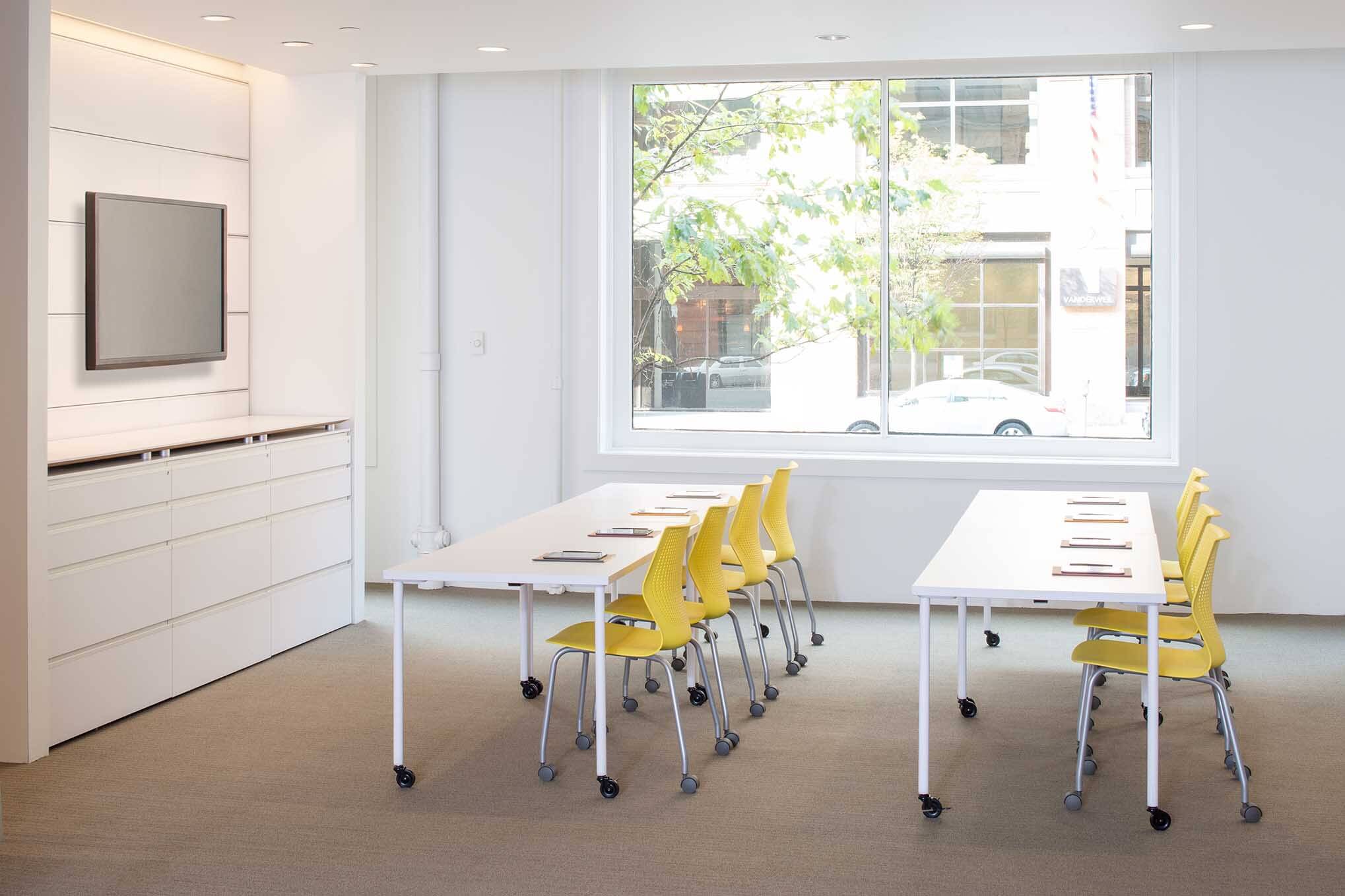 eight MultiGeneration Stacking Chairs in a white training room in two rows with rectangular white tables
