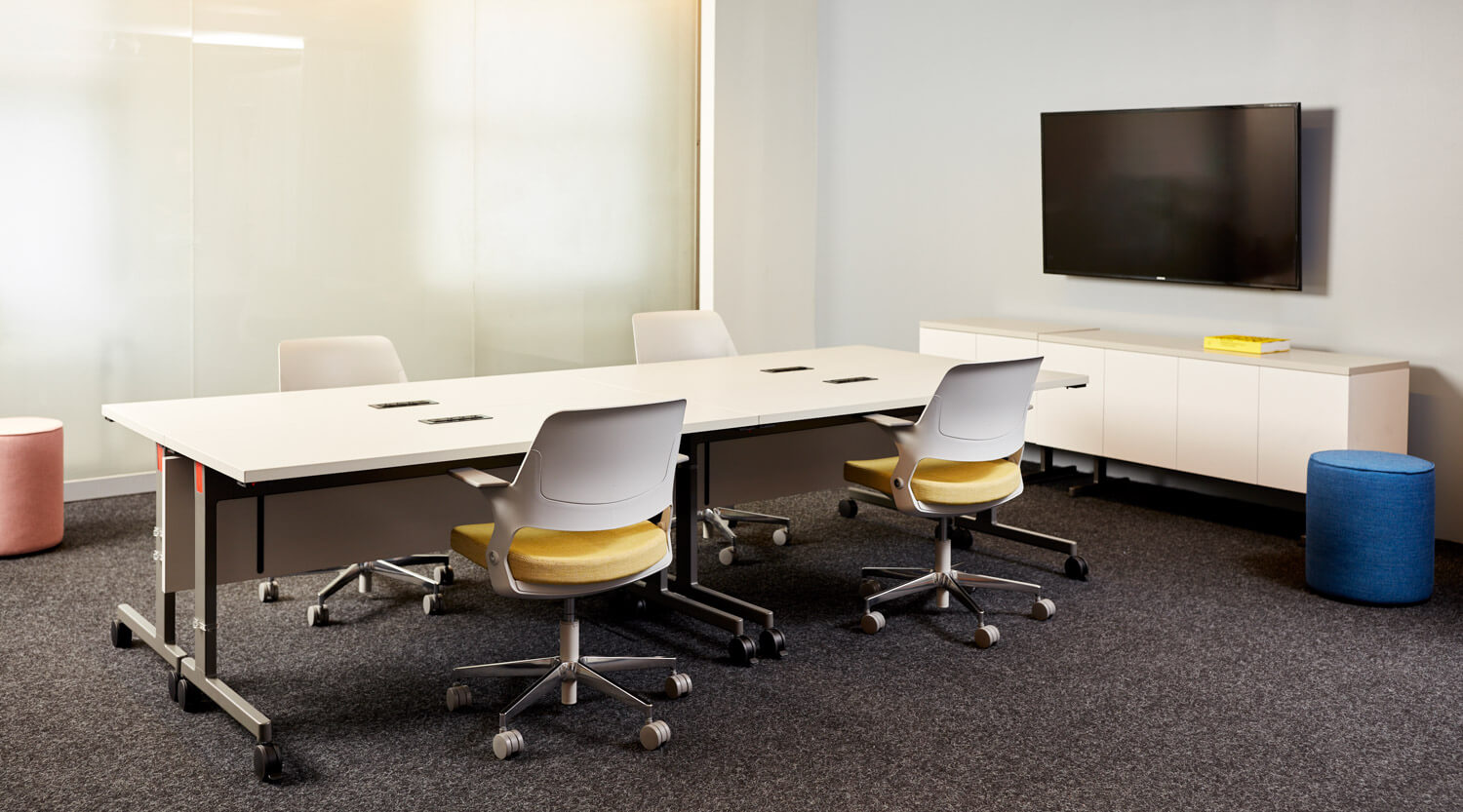 four Ollo Side Chairs in a meeting room around a white rectangular table and a tb in the wall
