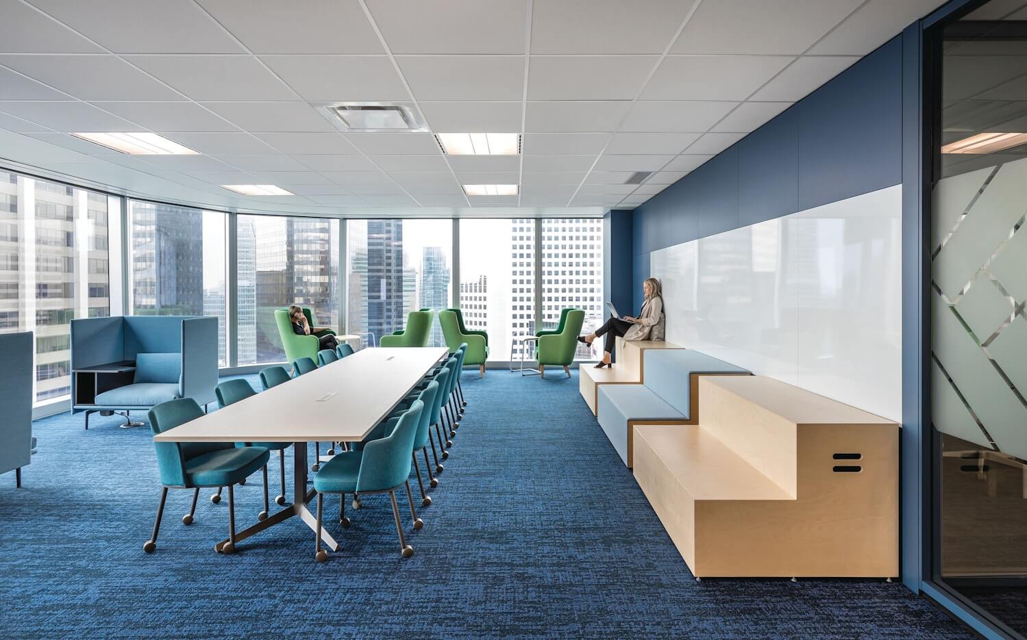 a modern common area at an office next a a big windows with city skyline featuring a long rectangular meeting room and remix side chairs areound the table 