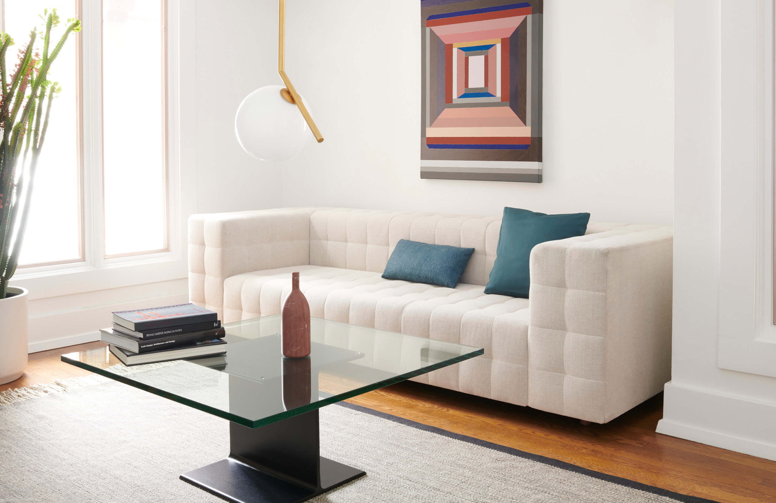 an I Beam Side Table in the middle of an elegant commercial space with a cream two seater sofa in a white room with a coloured minimalistic painting in the background