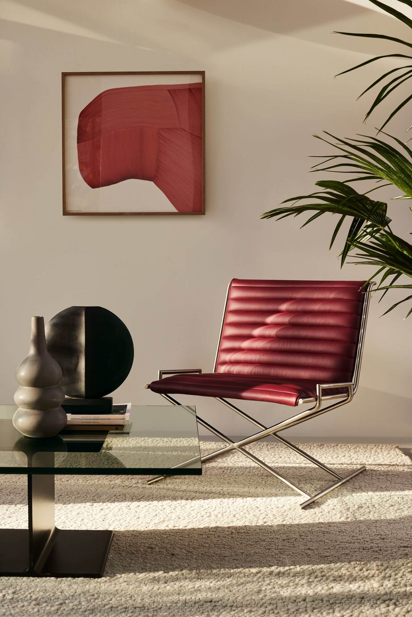 the front side of a glasstop I Beam Side Table in a cozy room with dim sunlight and a leather chair in the background