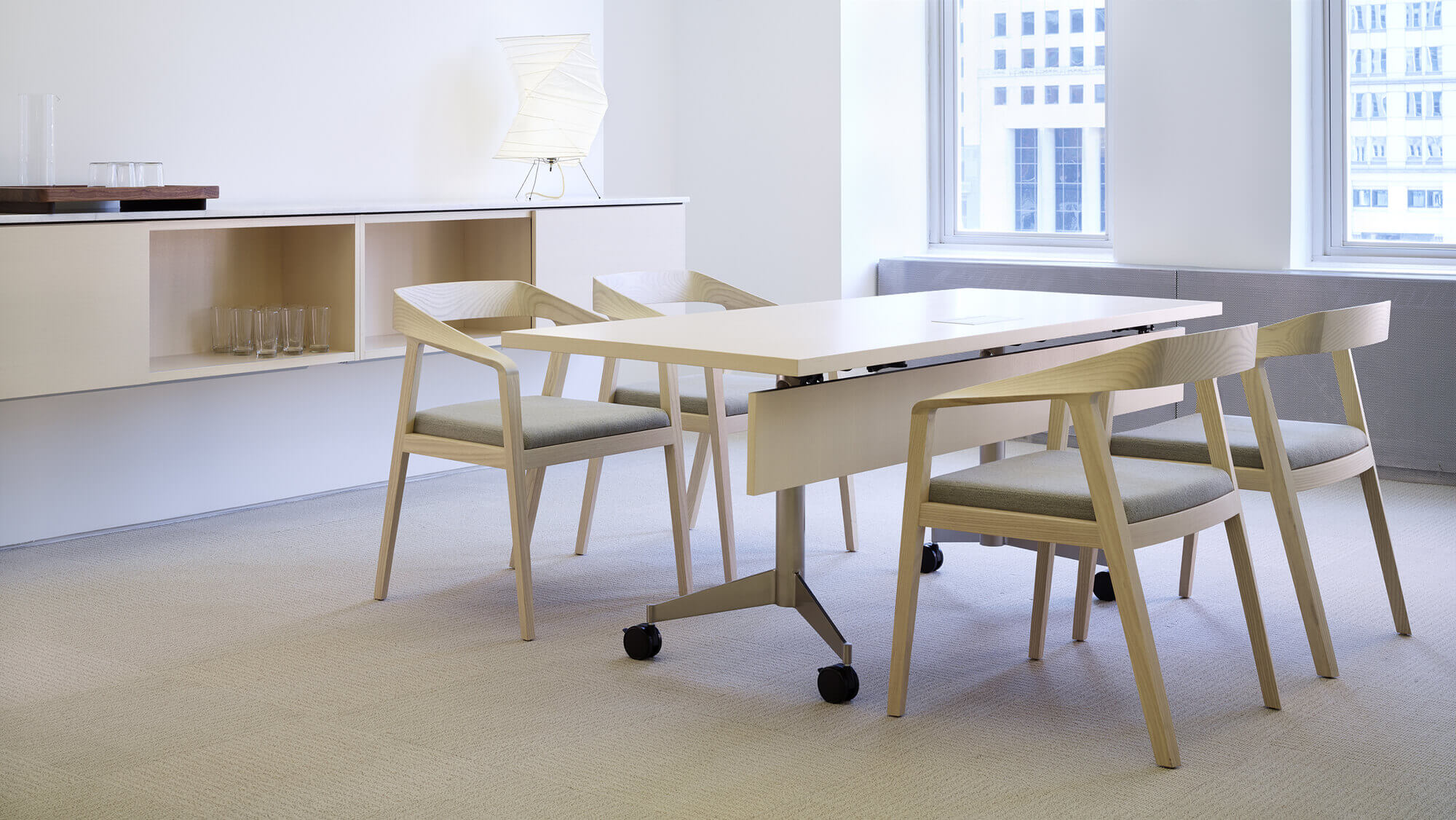 a wooden top MP Flex Training Table with four wooden chairs on the sides in a minimalistic office with two big windows on the right side