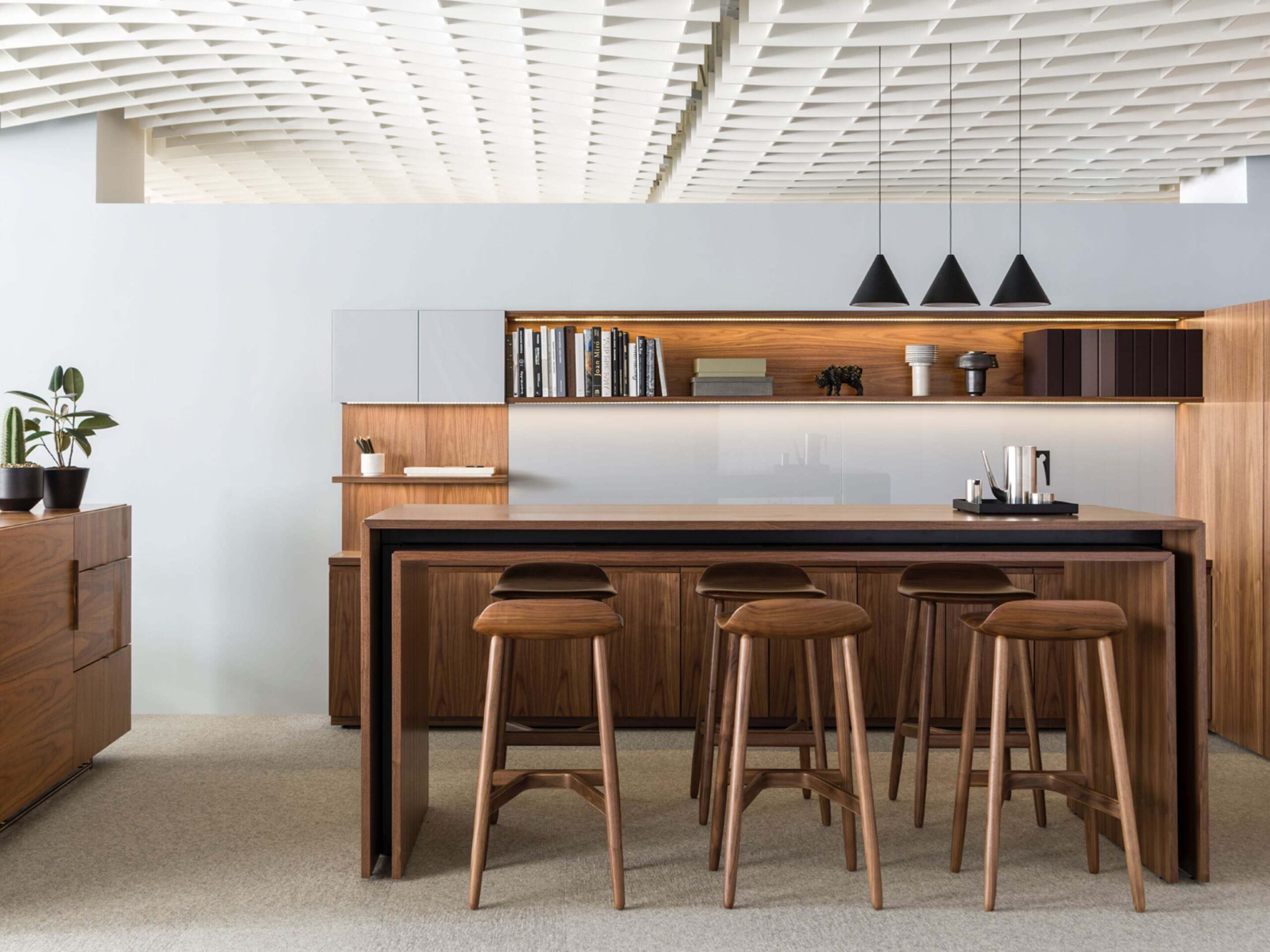 the front angle of a wooden white top Peer Conference Table featuring six wooden barstools on the sides and a modern wooden storage cabinet in the background