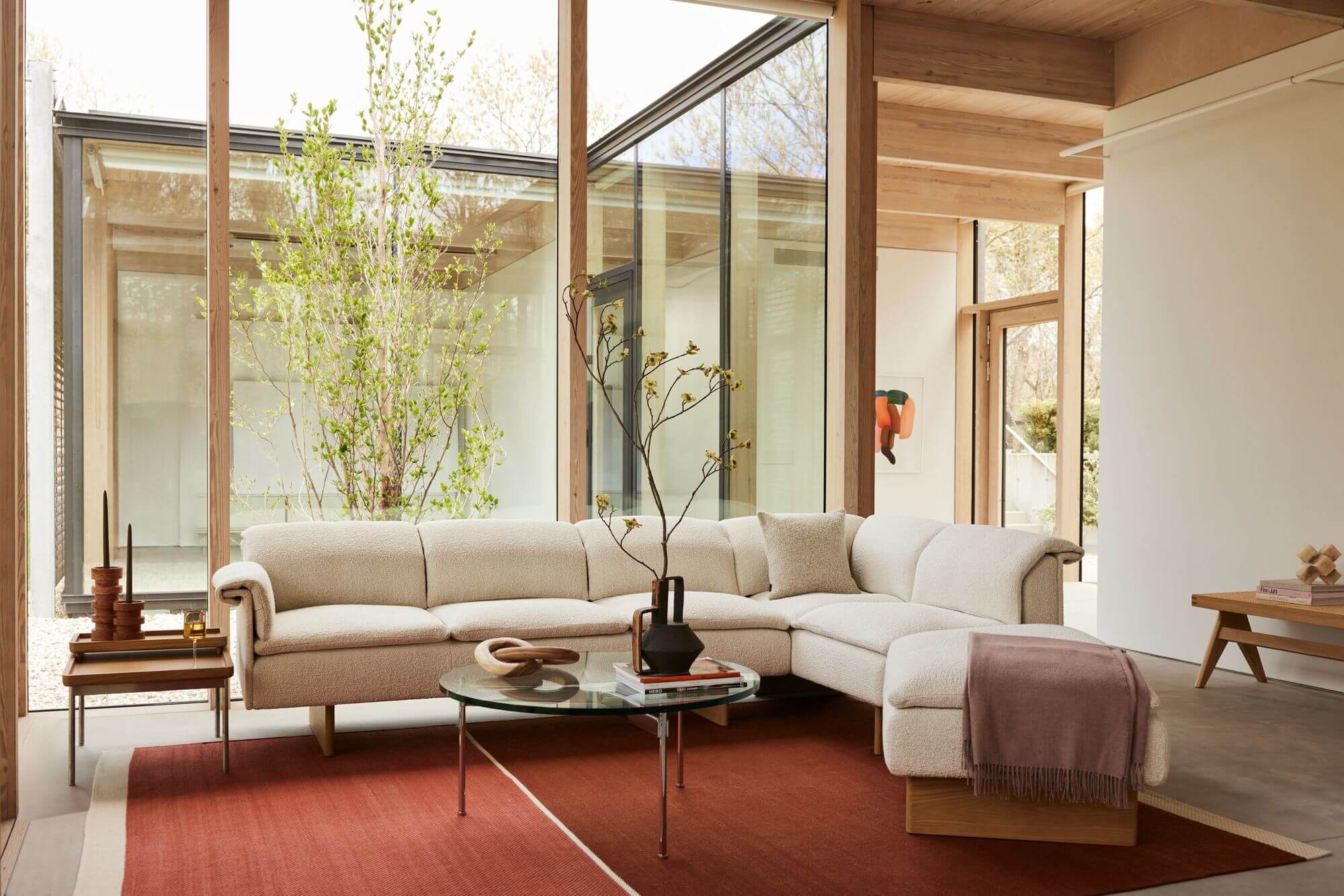 a modern livingroom with an L shaped sofa in cream colour and a rounded coffee table in the middle with a tuxedo side table on the left side next to a big window