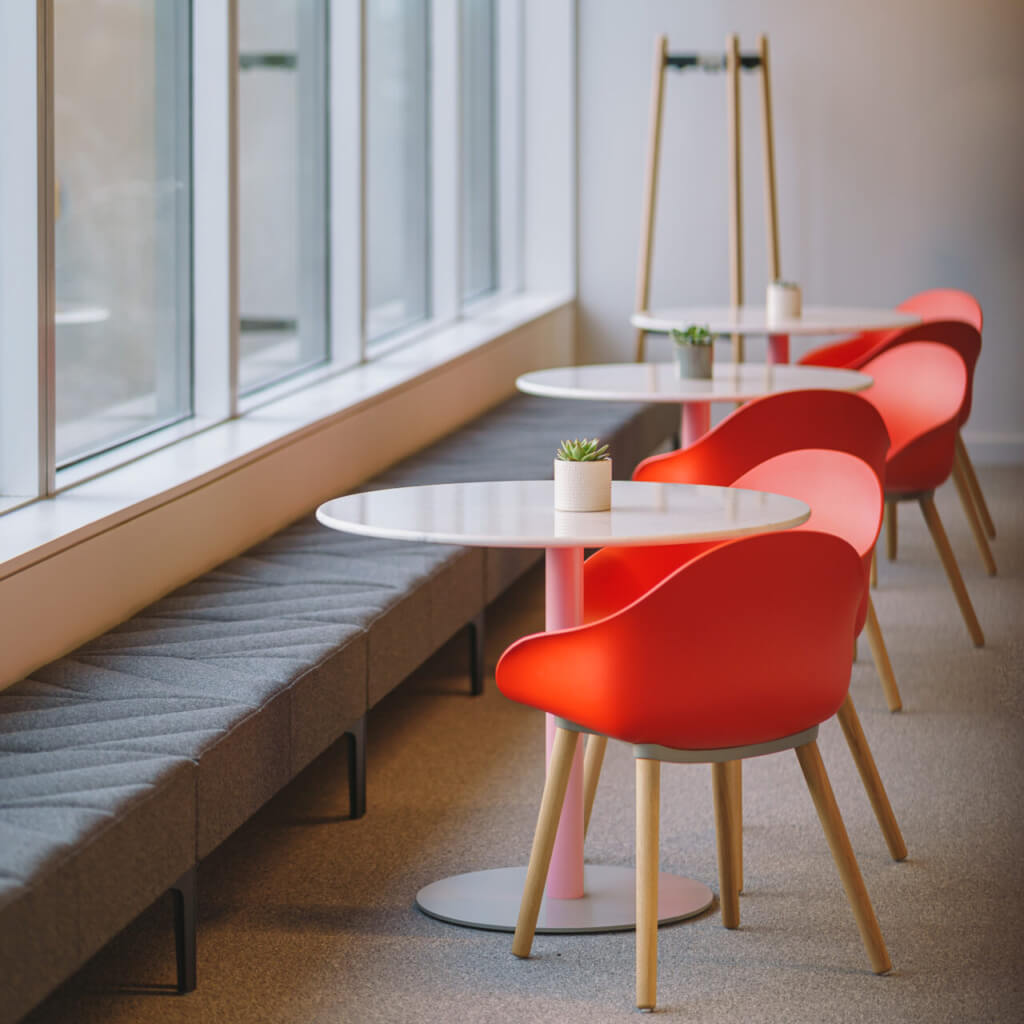 a modern shared commercial space featuring a line of Hatch Modular Sofas next to a big windows with side tables and red chairs.