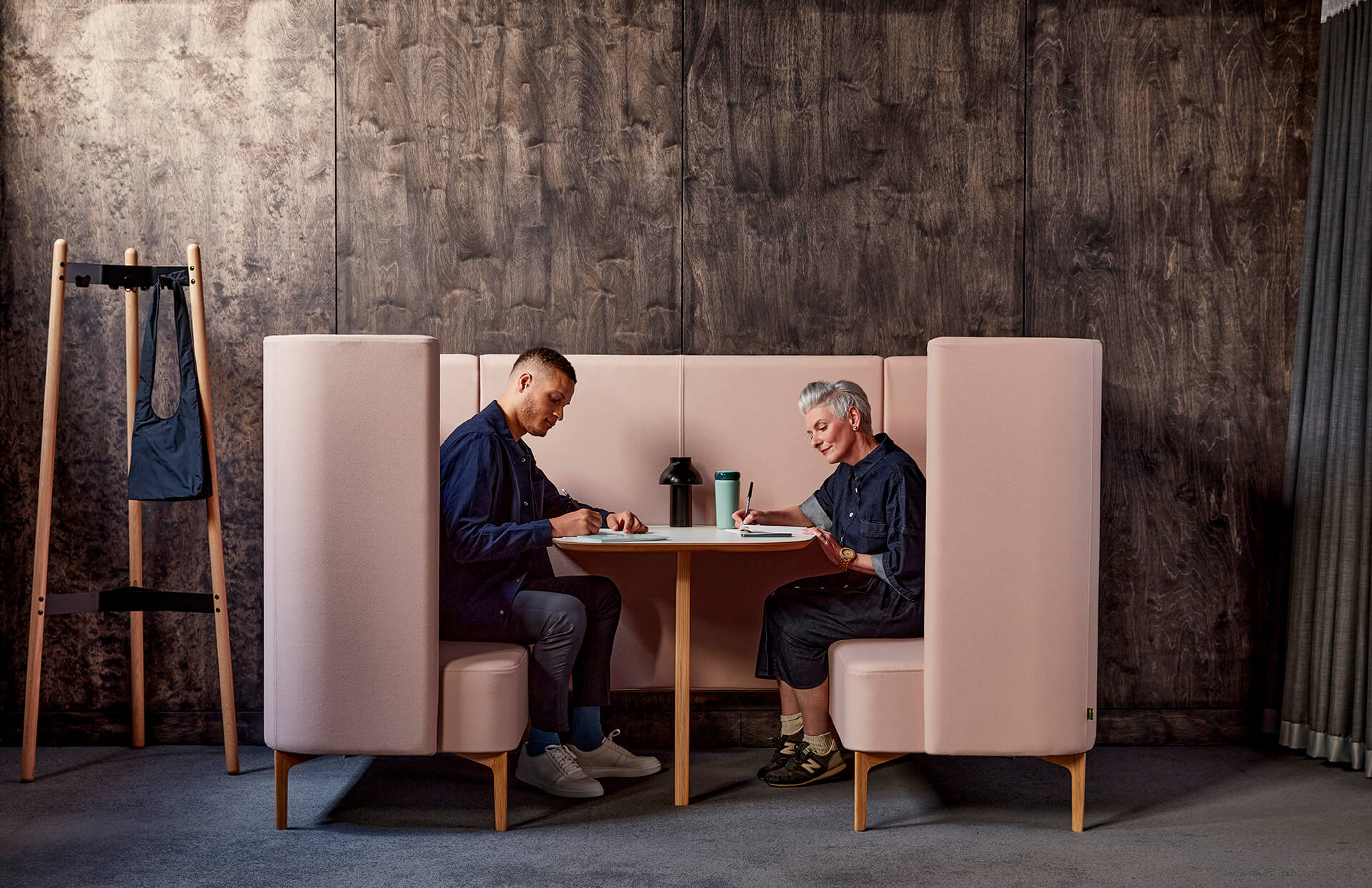 Hudson Coat Stand on the left side and a sofa booth on the right side with two people sitting on it