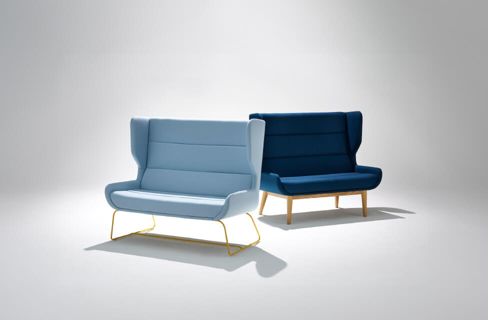two Hush High Back Sofas one in blue with wooden legs and ahother in light blue with metallic legs in a white room