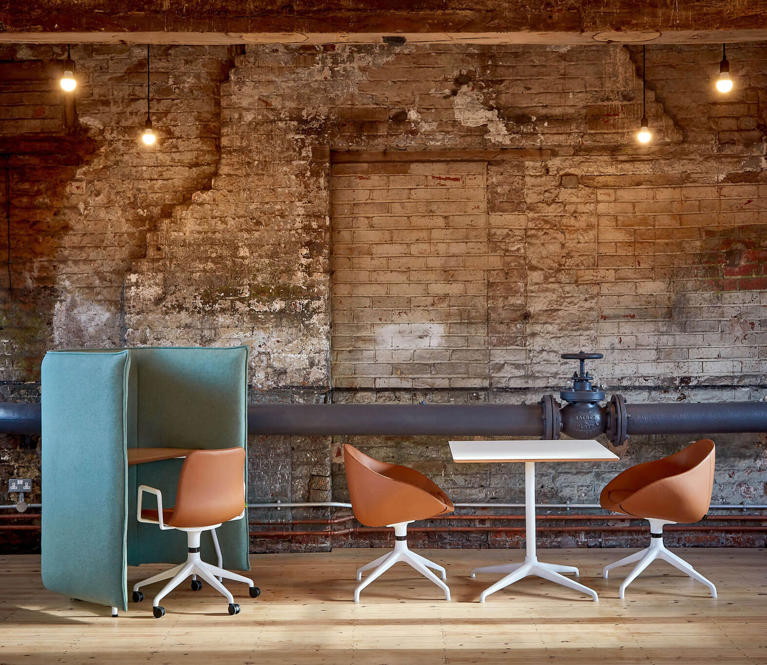 two always armchairs with brown leather upholstery at an modern minimalistic industrial office with a brick wall behind and a desk booth and chair on the left side