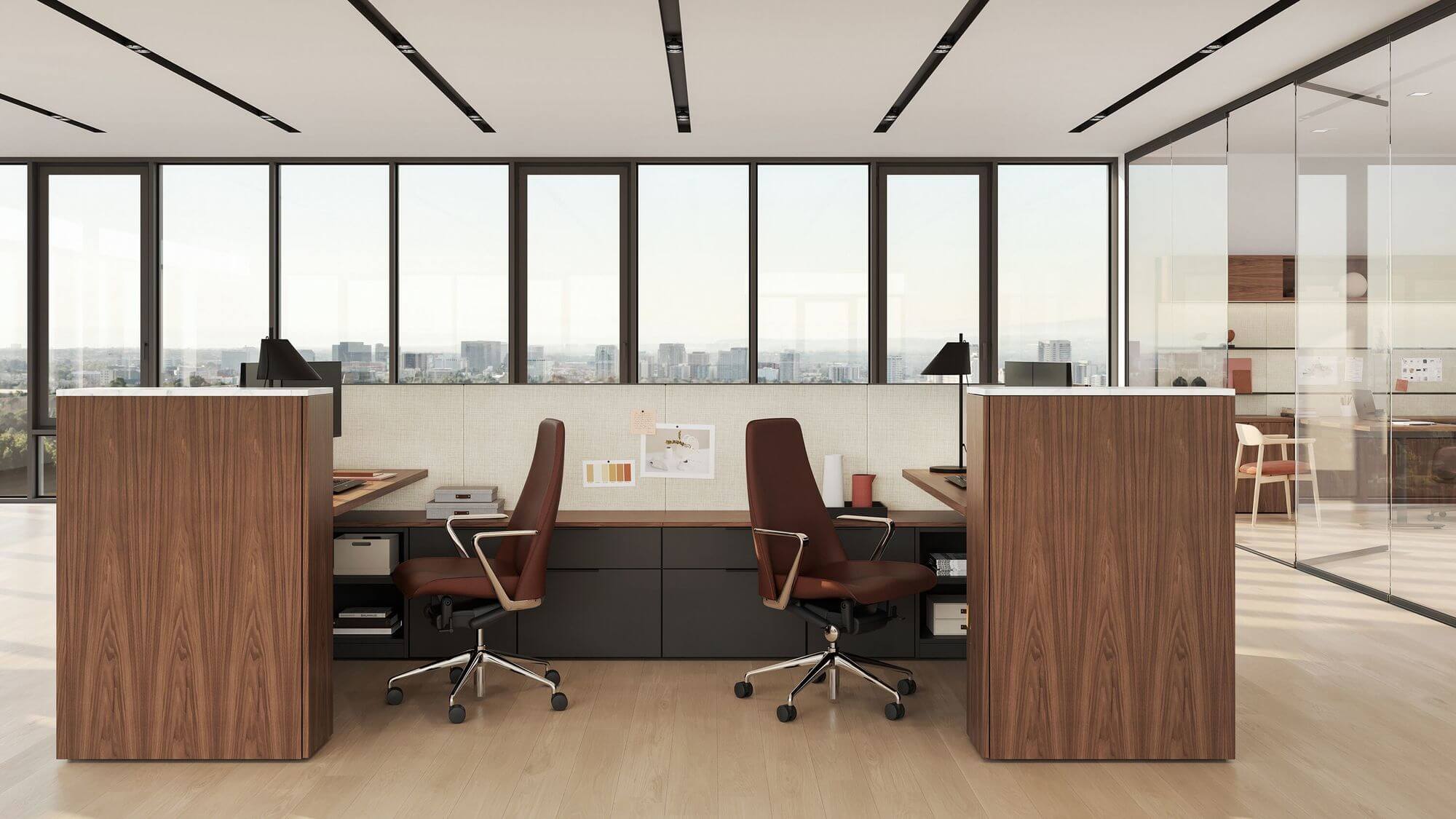 the front side of a two wooden geiger one open plan workstation with two executive chair and a monitor on top in a light room with wall windows in the background