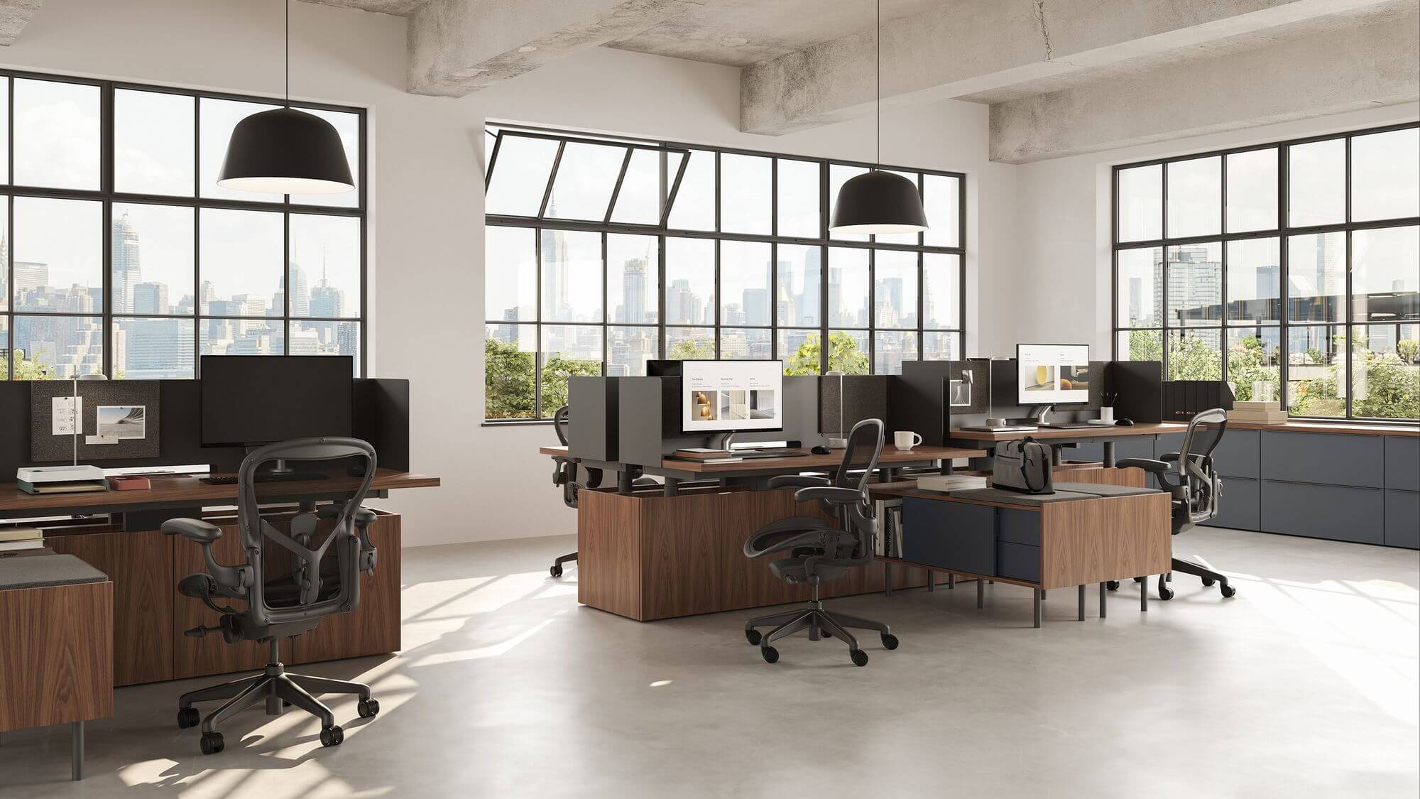 a modern office featuring four wooden geiger one open plan workstation with ergonomic chairs and a monitors on top in a light room with big windows in the background
