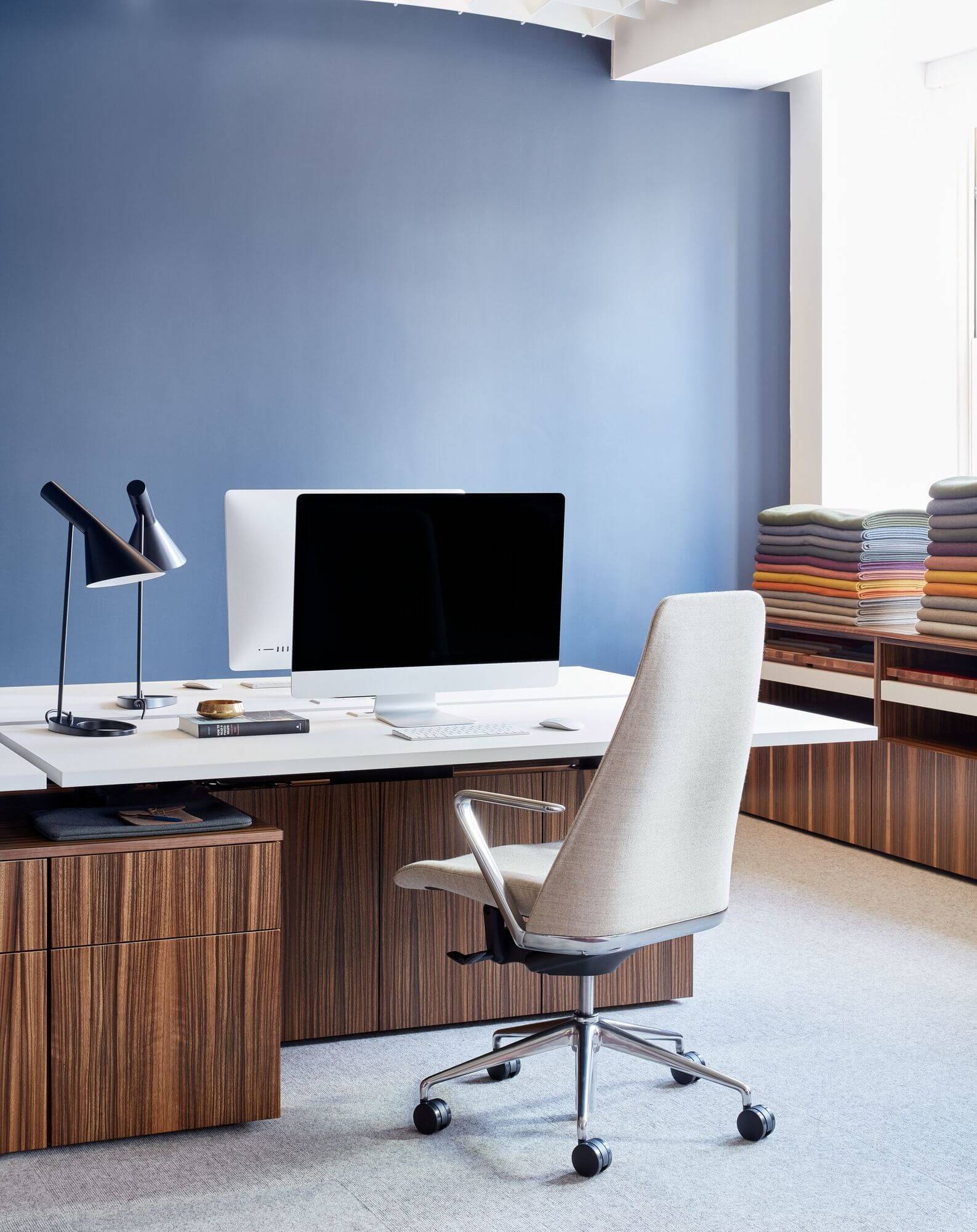 the right side of a wooden geiger one open plan workstation with an executive chair and a monitor on top in a light blue room