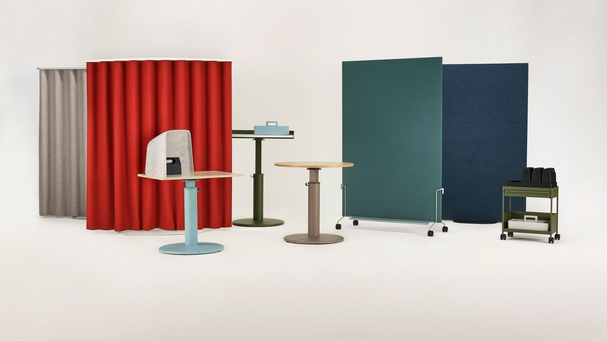 a set of coloured furniture in a white room featuring oe1 sit to stand tables, a storage unit and space division panels in the background in a light green room