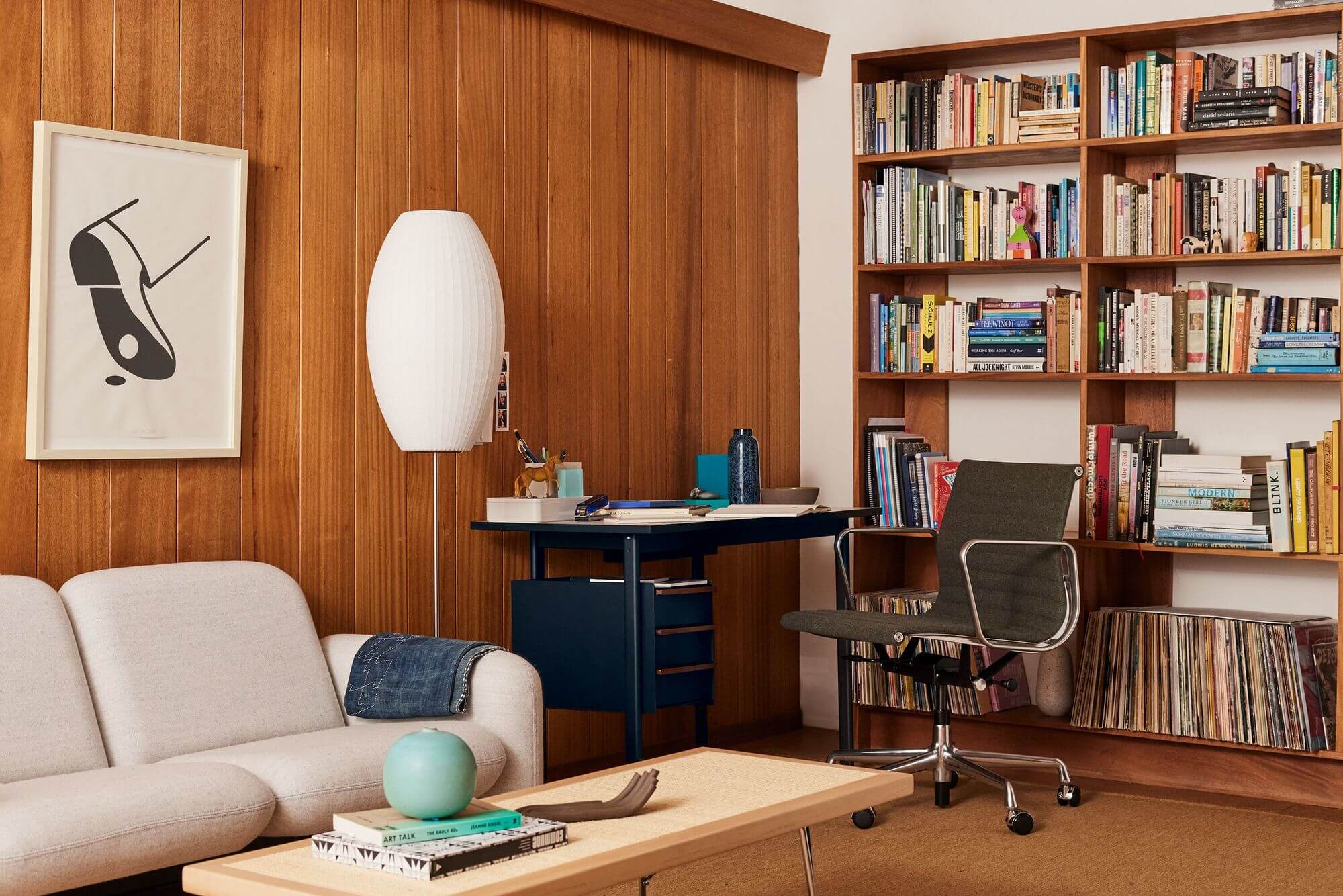 a stylish home office setting featuring a side chair a sofa and a Mode Wooden Top Desk with a book shelf in the background