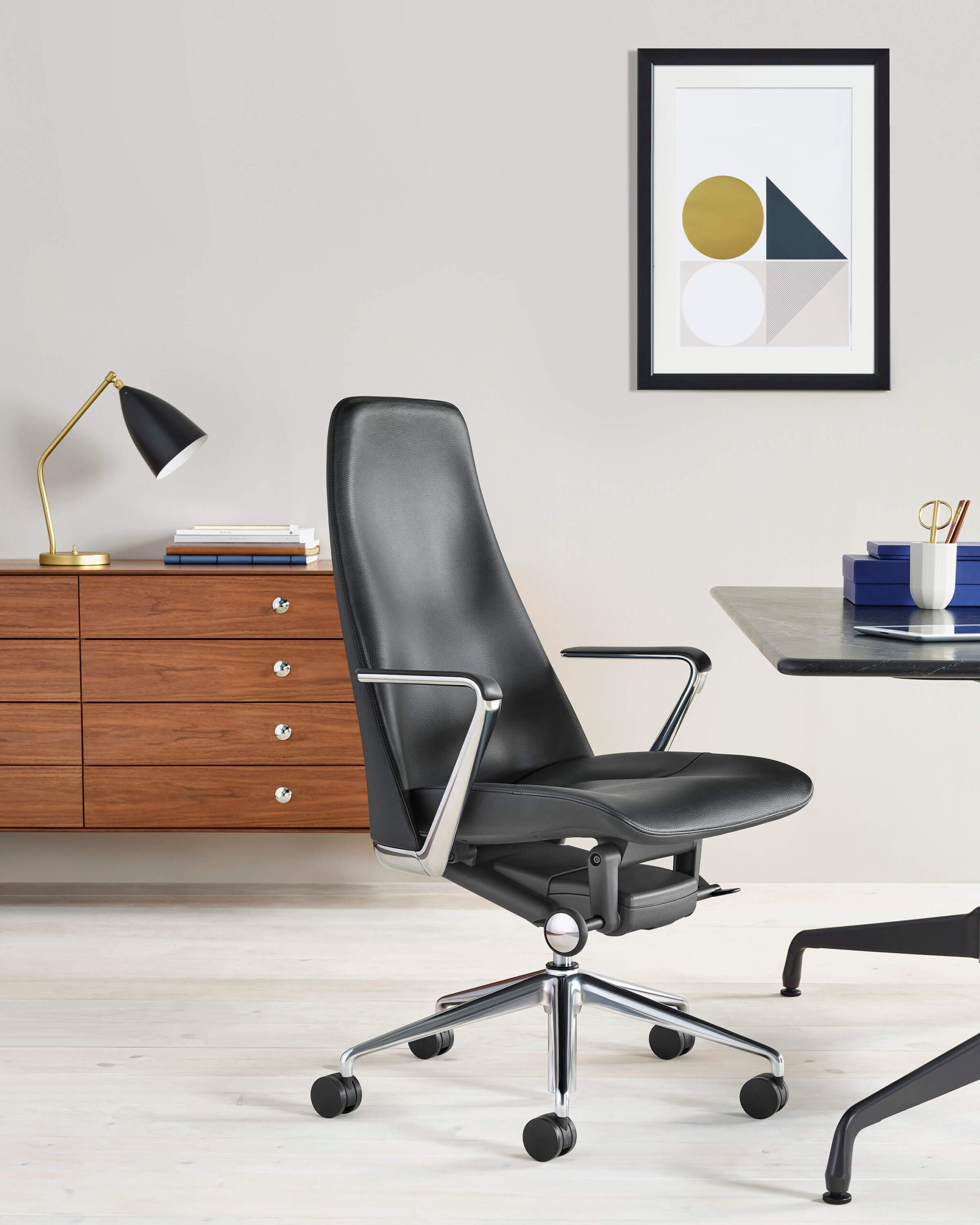 a minimalistic office featuring a Nelson Thin Edge Storage Buffet in the background and a leather office chair in the front next to a desk
