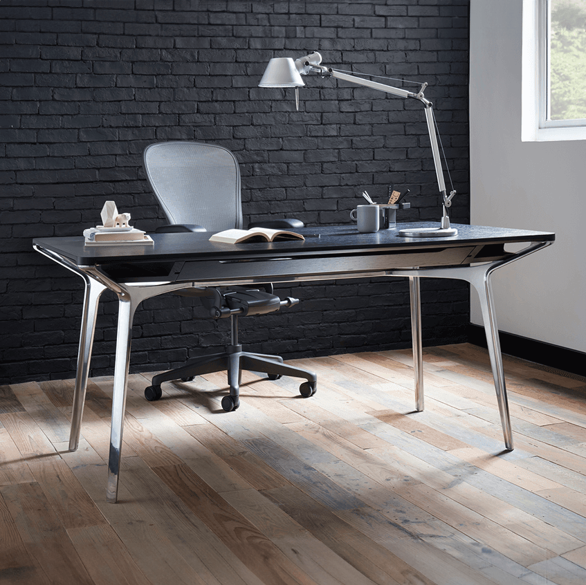 a carafe table designed bybthe australian furniture designer Charles Wilson for herman miller in a modern home office with a lamp on top and a desk chair in the background, with a window in the right.