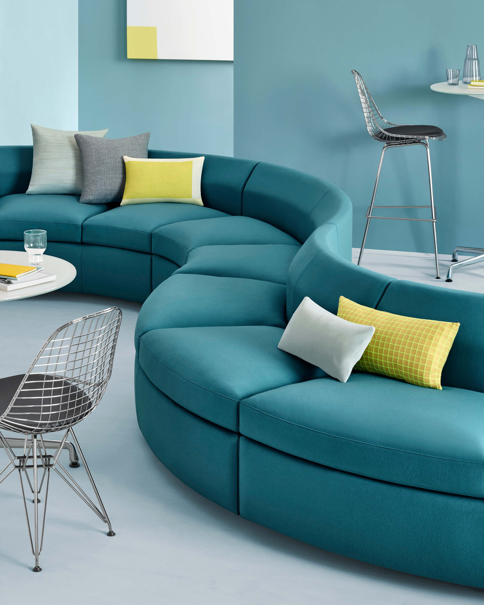 the side detail of a teal S shapped Bevel Modular Sofa Group in a modern office room with two side tables and for wired chairs around