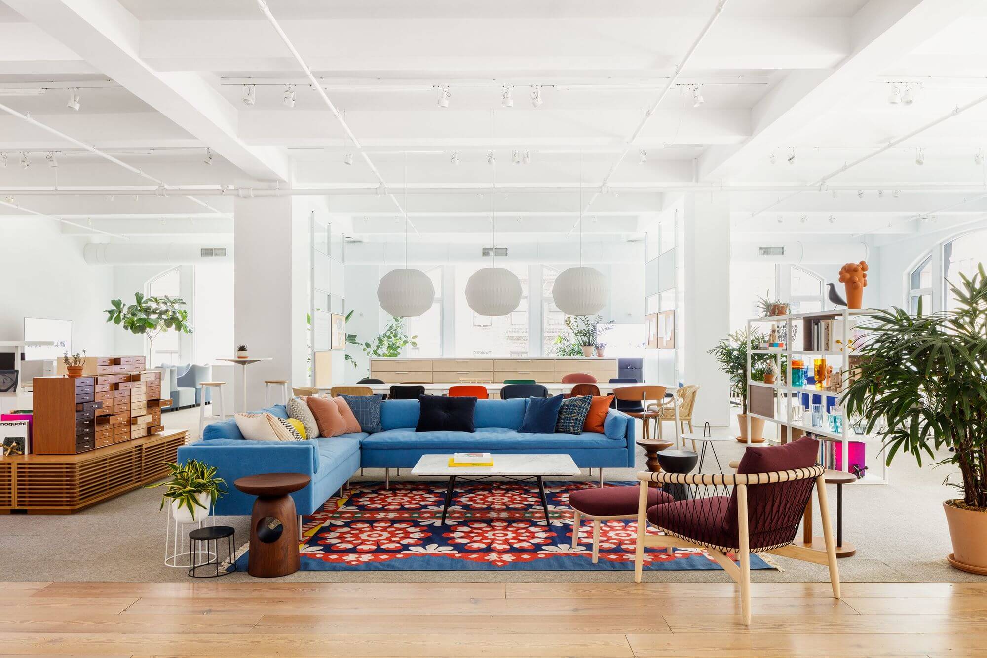 the front side angle of an L shapped blue Bolster Sofa Group in the middle of a colourful commercial space with white walls and tall windows.