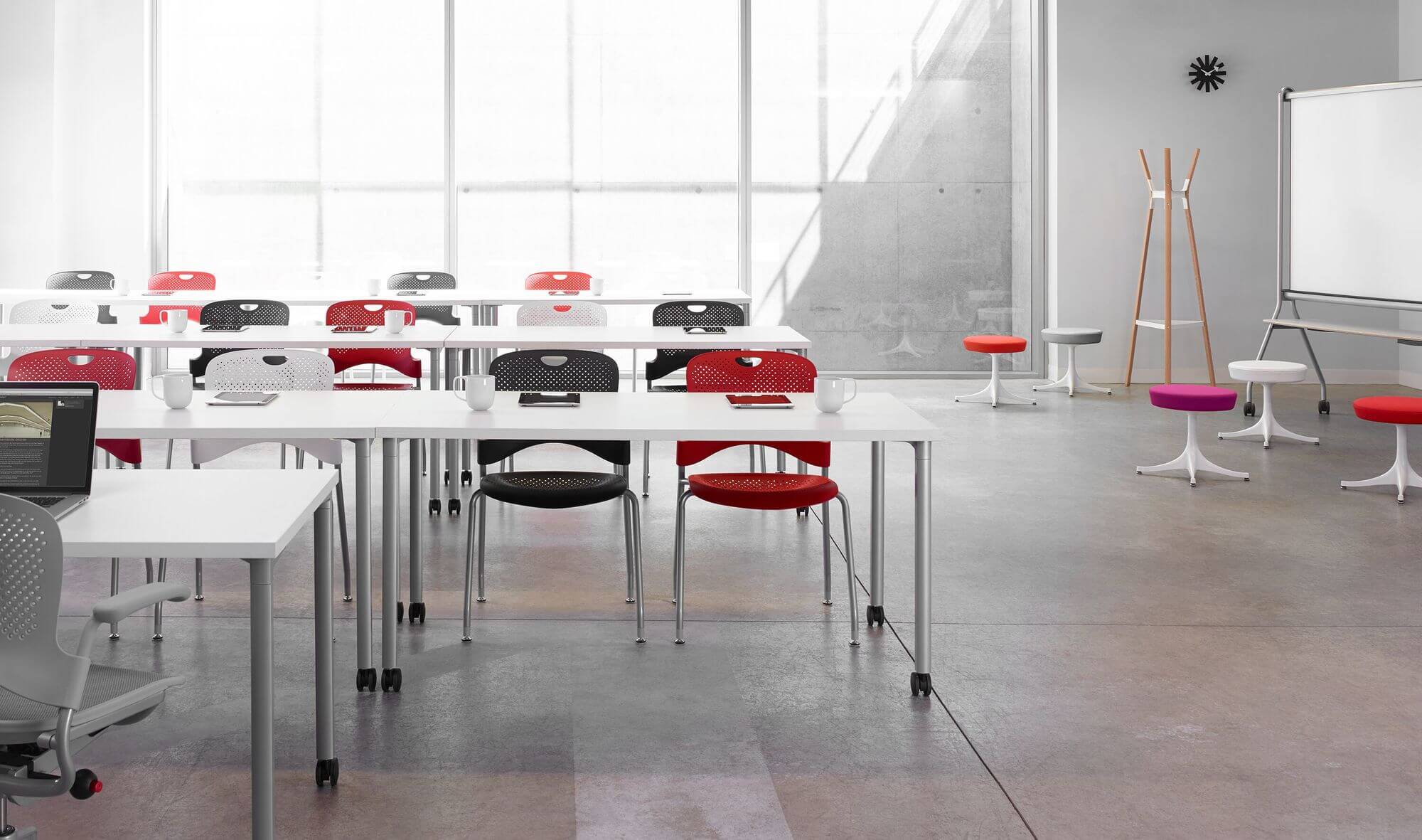 a modern white classroom with concrete walls featuring thre rows of student chairs and Everywhere Multi-Purpose Tables and a whiteboard in the right side