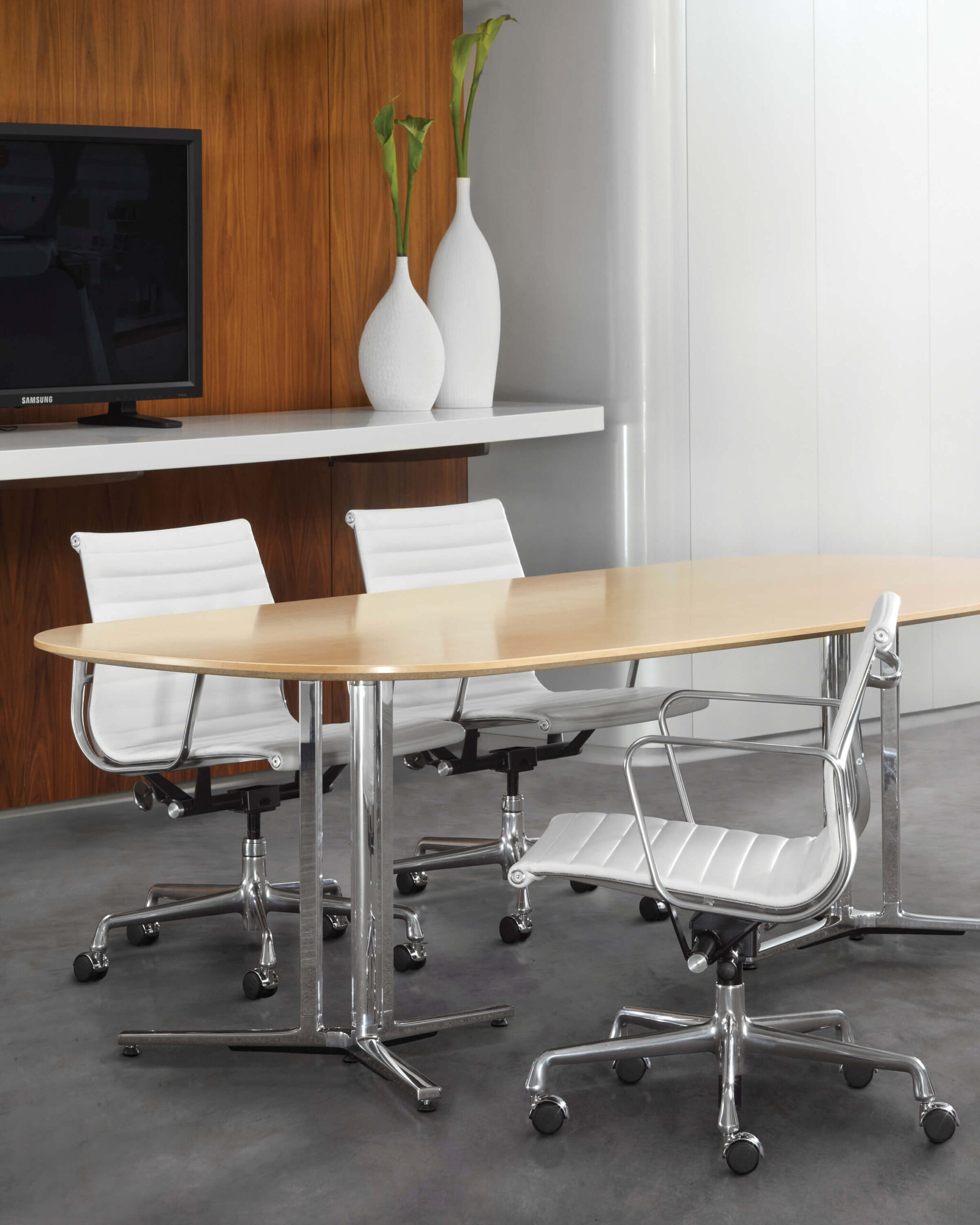a modern meeting room with a tv in the back ground a a wooden top Everywhere Multi-Purpose Tables in the middle surounded by three white leather chairs