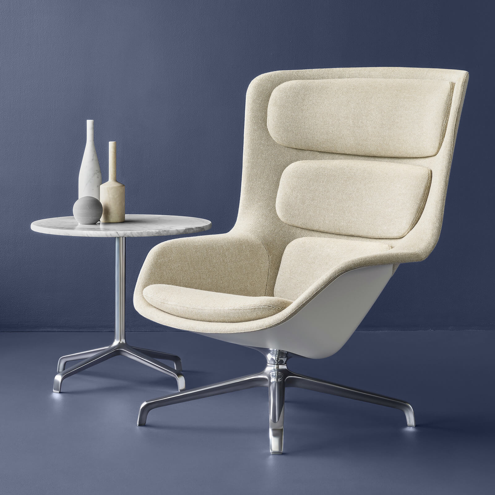 a high back Striad Lounge Chair with cream upholstery and a marble side table in an ocean blue room