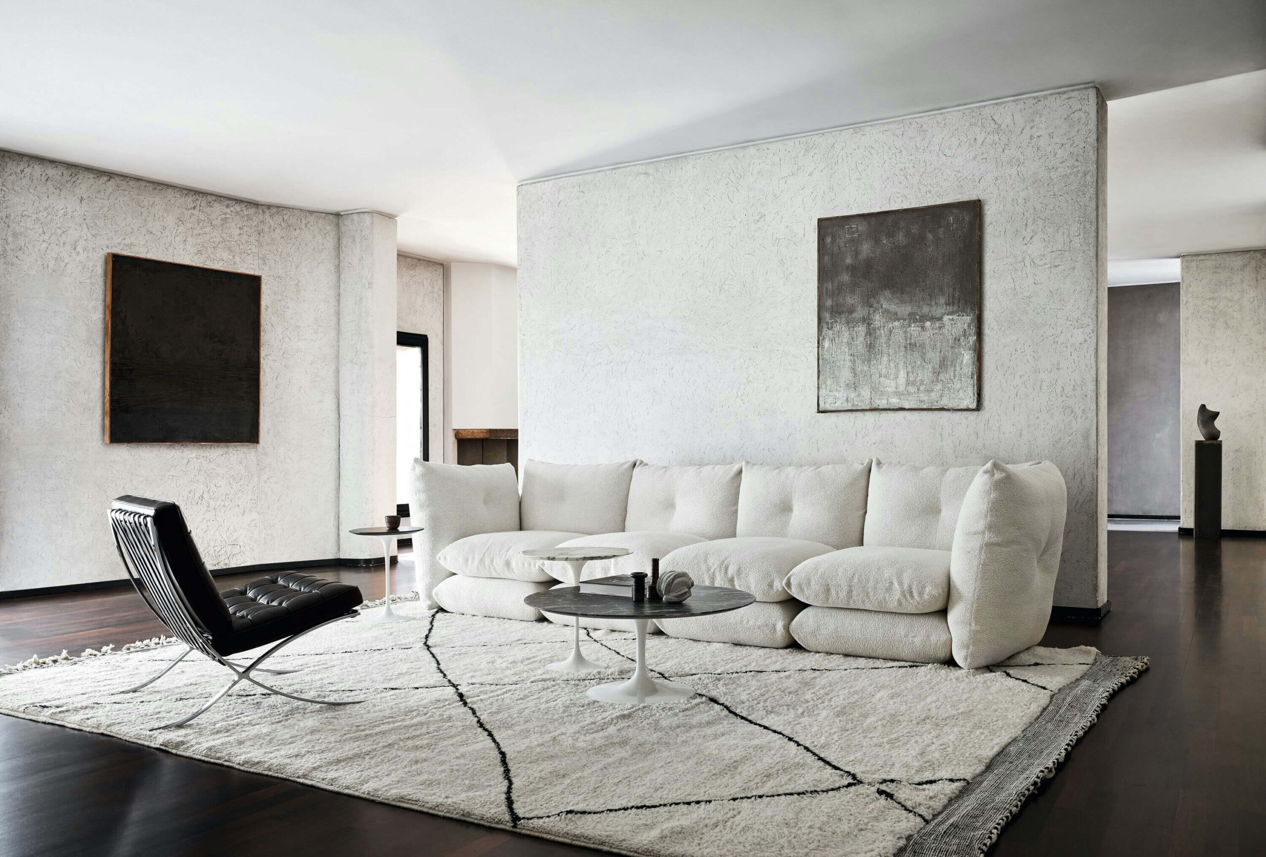 a minimalistic livingroom featuring a white perron pillo sofa by knoll in the middle next to a coffee table and a leather chair in the corner