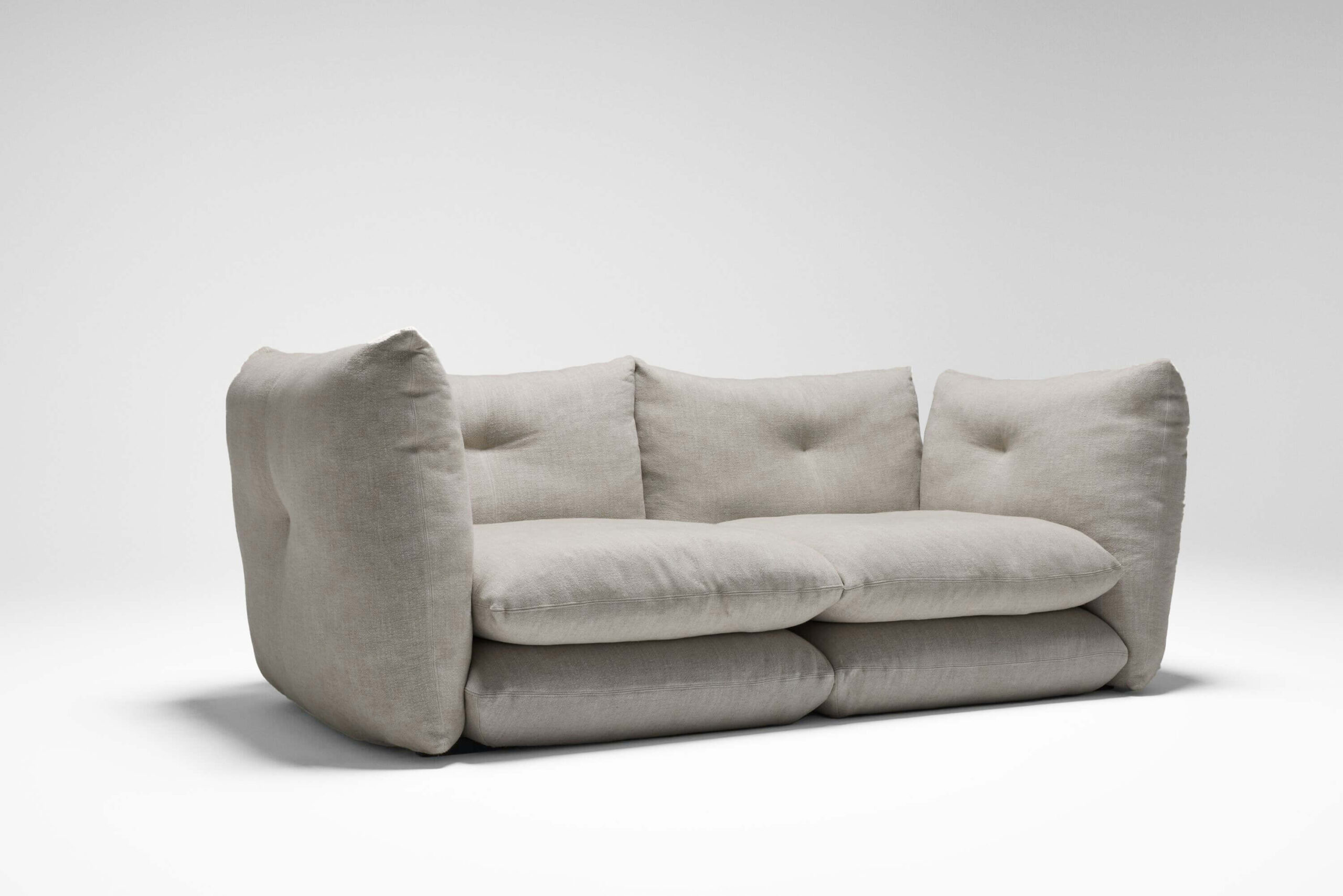 the left side angle of a two seatter perron pillo sofa by knoll with light gray upholstery in a white room