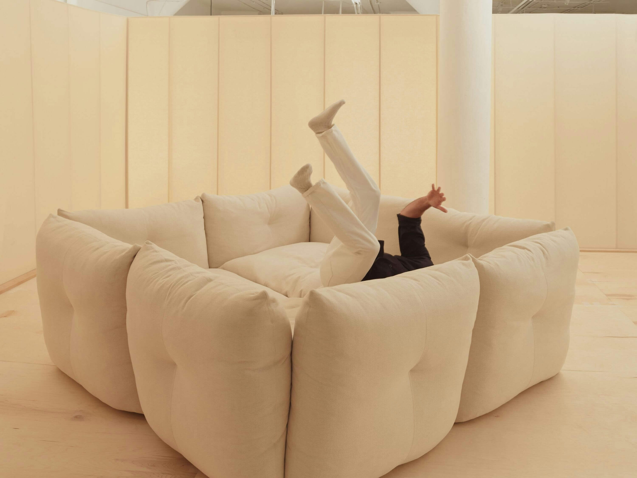 the side angle view of an square shapped perron pillo sofa in a room with warm lights and a person jumping in the middle of the seats