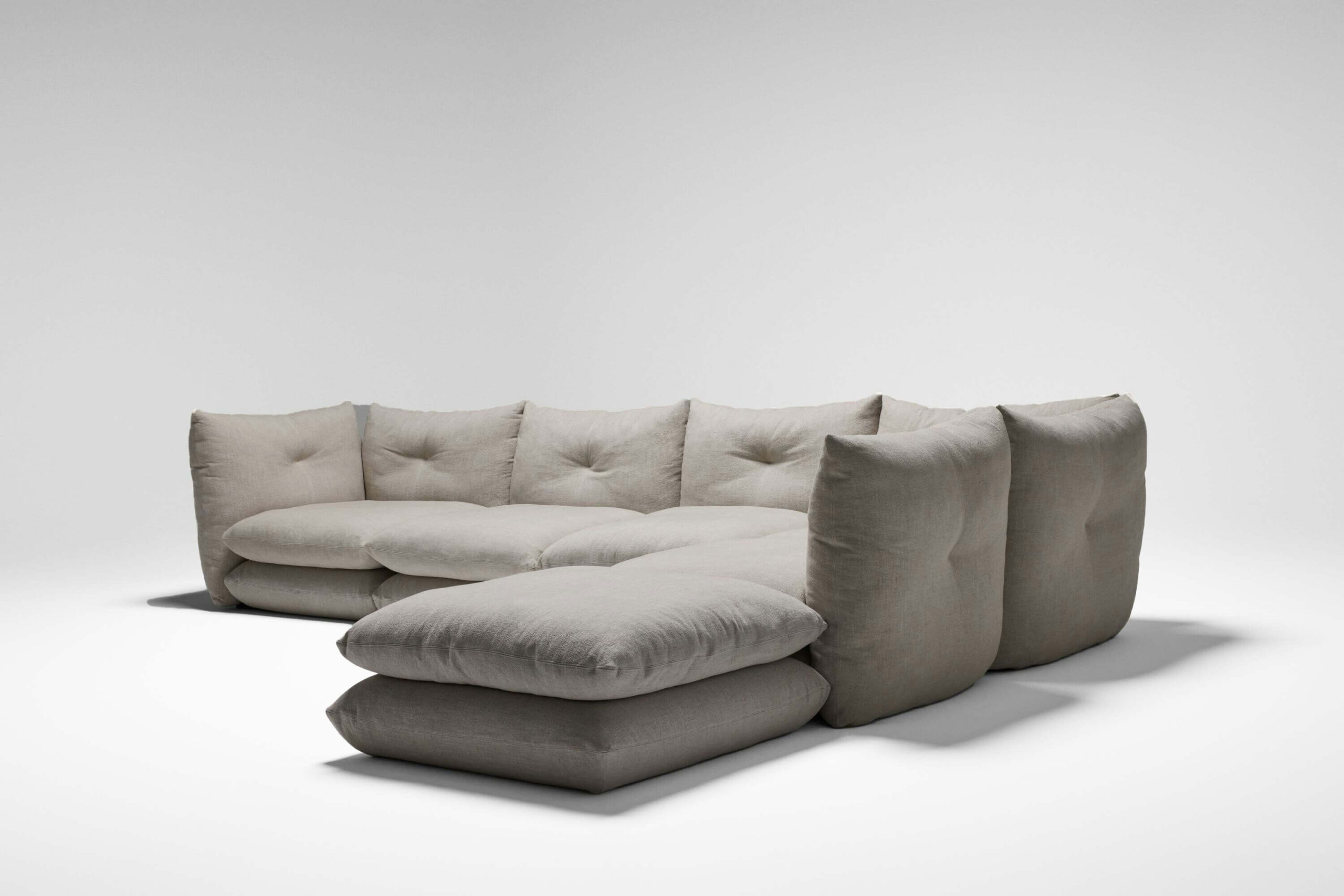 the close up of the right side of a five seat L shapped perron pillo sofa by knoll with light gray upholstery in a white room